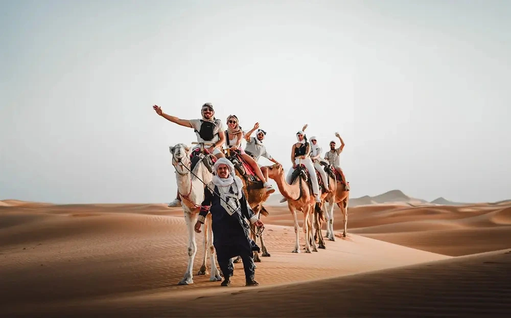 Group of travelers enjoying camel ride during shared desert tour from Marrakech to Merzouga Sahara Morocco